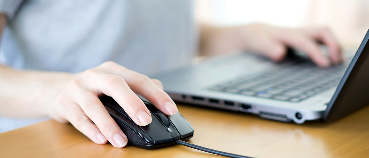 Zwei Hände bedienen Laptop und Maus an einem Schreibtisch