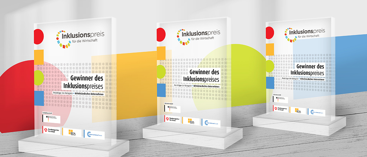 Drei Inklusionspreis-Trophäen stehen vor dem Hintergrund, der bunte Elemente des Logos aufgreift