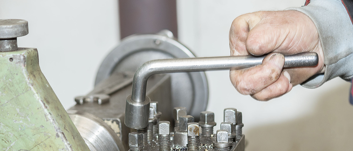 Eine Hand mit fehlenden Fingern bearbeitet eine Maschine mit einem Drehkreuzschlüssel