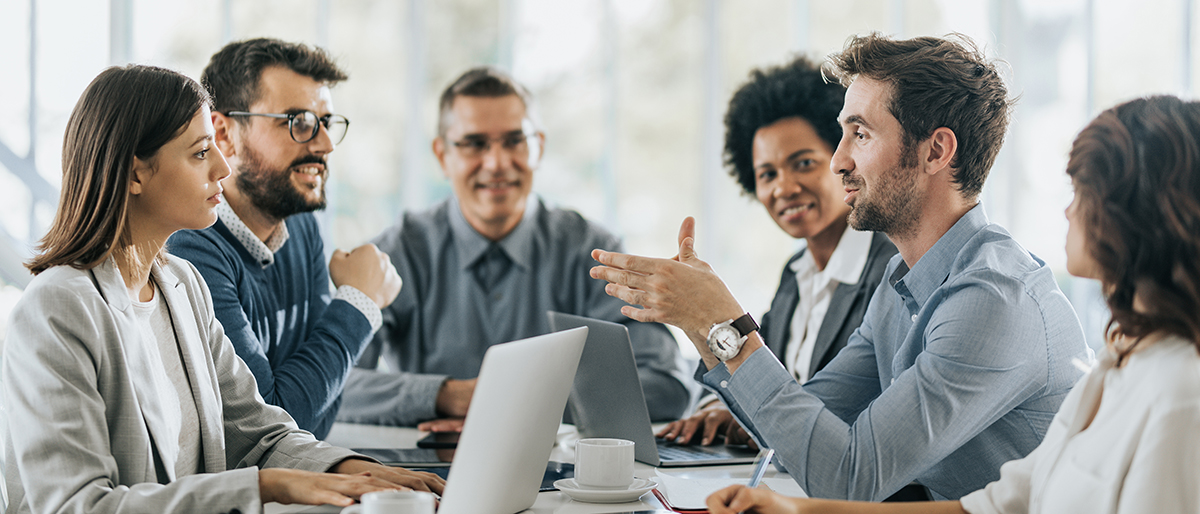 Gruppe von Menschen am Konferenztisch, ein Mann erklärt etwas