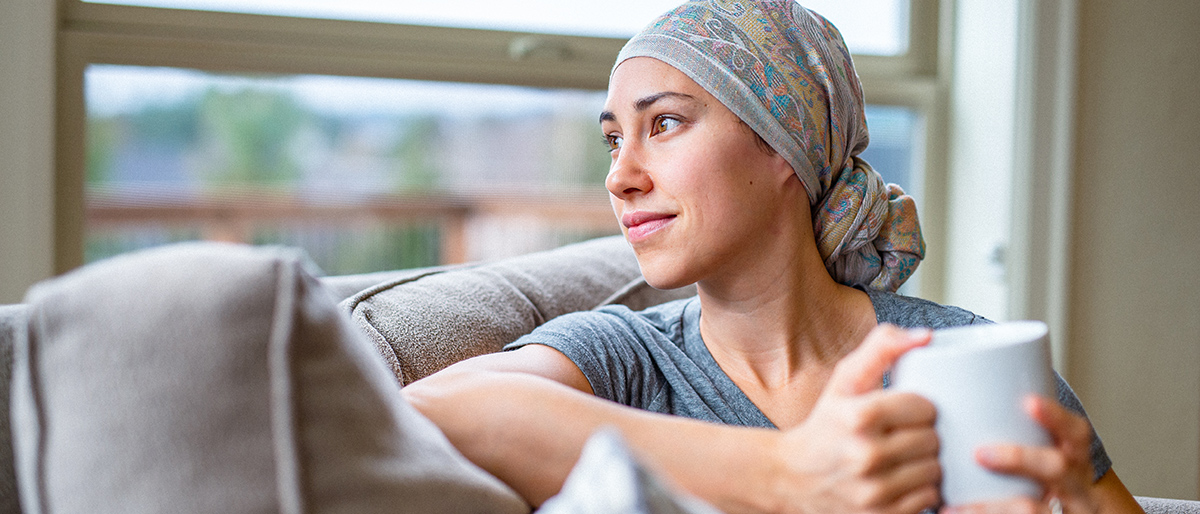 Frau mit Kopftuch sitz mit Tass auf Ihrem Sofa.